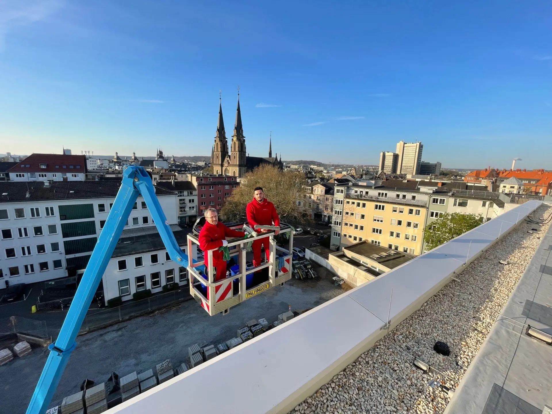 Zwei WSR-Mitarbeiter auf einer Hebebühne bei der Glasreinigung, im Hintergrund die Bonner Innenstadt